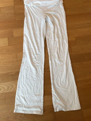 Vita mjukisbyxor från Gina Tricot - Vita mjukisbyxor från Gina Tricot med utsvängda ben och hög midja. Byxorna är tillverkade i ett mjukt och stretchigt material som är skönt att ha på sig. Perfekta för en avslappnad och chill look.