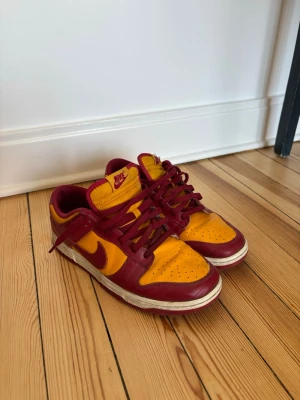 Nike Dunk Low röd/gul sneakers - Säljer ett par Nike Dunk Low sneakers i rött och gult läder med klassisk Swoosh på sidan. Kallas Midas gold/tough red. 