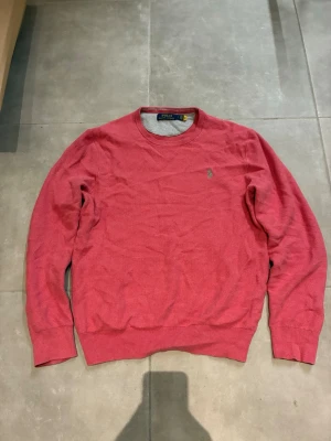Pink ralph lauren - Säljer en rosa stickad tröja från Polo Ralph Lauren med rund halsringning och diskret broderad logga på bröstet. Tröjan har ribbade muddar vid ärmslut och nederkant. Perfekt för dig som gillar klassisk och stilren design.