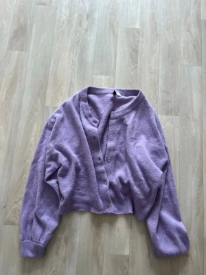 Ljuslila kofta från H&M Divided - PASSAR S OCH M. Mysig ljuslila kofta från H&M Divided med rund halsringning och knappar framtill. Koftan är croppad och har långa ärmar med ribbade muddar. Perfekt för att addera färg till din outfit.