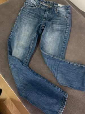 Blå raka jeans från Lager 157 - Snygga blå jeans från lager 157 med klassisk rak passform och fem fickor. Jeansen har en lätt tvättad look med slitningar på låren och bakfickor med lager -logga. Tillverkade i slitstark denim som passar perfekt till en avslappnad stil.