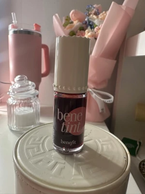 Benetint flytande rouge från Benefit - Benetint från Benefit är ett flytande rouge i en djup rosaröd nyans. Kommer i en liten glasflaska med vit, räfflad skruvkork dekorerad med pärldetaljer. Perfekt för att ge kinderna en naturlig, fräsch färg. Kan även användas på läpparna.