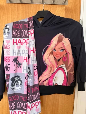 Pyjamas - pyjamas,  svart hoodie med tryck på framsidan. Byxorna har mönster med text och tecknade figurer i rosa, och vitt. Barn storlek! Storlekslappen blev avklippt. Storlek 128-137