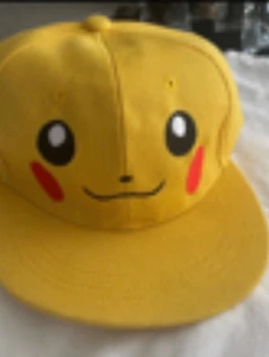Gul Pikachu keps med tryck - Säljer en gul keps med Pikachu-motiv från Pokémon. Kepsen har platt skärm och Pikachus ansikte tryckt framtill med svarta, vita och röda detaljer. Perfekt för dig som gillar anime och vill sticka ut med en färgglad accessoar. Stlk kvar 3-7 år och 8 år + 