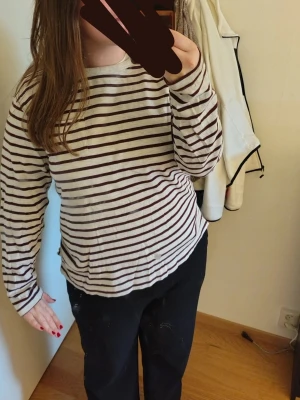 Randig långärmad tröja grå/vinröd - Säljer en långärmad tröja med ljusgrå botten och vinröda horisontella ränder. Tröjan har en avslappnad passform och är tillverkad i mjukt stickat material. Perfekt för en chill och enkel stil. Storlek L. Egentligen herr, men passar även för dam. 