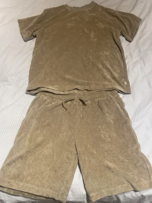Beige set i frotté från grunt - Säljer ett beige set från grunt i mjuk frotté. Setet består av en t-shirt med rund hals och ett par shorts med dragsko och fickor. Perfekt för chill dagar hemma eller på semestern. Materialet är skönt och andas bra.