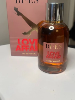 BI-ES Love Affair Eau de Parfum - BI-ES Love Affair Eau de Parfum kommer i en rund glasflaska med silverfärgad kork och rosa etikett. Doften presenteras i en matchande rosa kartong med guld- och röda detaljer. Perfekt för dig som gillar eleganta och moderna parfymer.