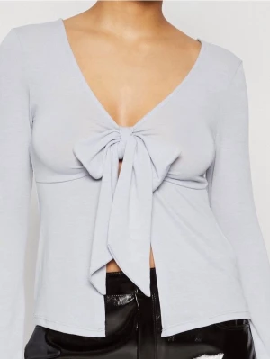 Ljusblå topp med knyt framtill - Trendig ljusblå topp med lång ärm och djup v-ringning. Toppen har en snygg knyt-detalj framtill som ger en feminin touch. Tillverkad i mjukt material som sitter skönt på kroppen. Perfekt för dig som vill ha en unik och stilren look. Använd en enstaka gång, inga defekter eller liknande.