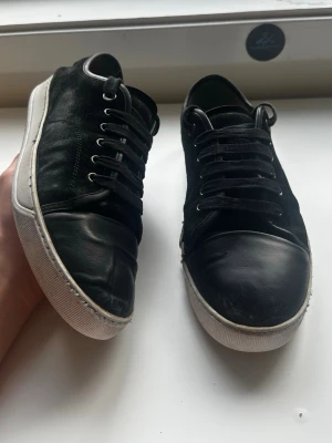 Svarta lanvins - Svarta mockaskor med blank cap toe från Lanvin, modell DBB1, storlek UK 8 (ungefär EU 42–43). Skorna är i bra skick, med två mindre defekter: vissa sömmar har gått upp och det finns ett hål i sulan, men en formad plastpåse fungerar som skydd, så de är fortfarande fullt användbara. Nypris ligger på 4499 kr. Inga originaltillbehör medföljer.  Kolla gärna in profilen också, där finns flera märkeskläder och skor – du hittar säkert något mer som passar 😉💯 Hör av dig om du undrar något!