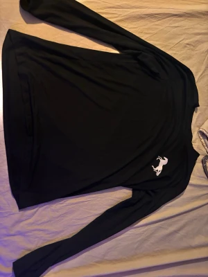 Svart långärmad tröja med tryck - Svart långärmad tröja med en vit hästlogga på bröstet. Tröjan har enkel och stilren design, rund halsringning och är gjord i ett mjukt material som känns skönt mot huden. Perfekt för dig som gillar minimalistisk stil.