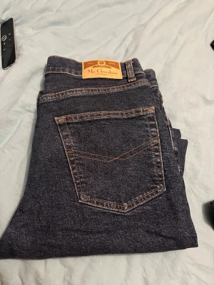 Mörkblå jeans från Mc Gordon - Säljer ett par klassiska mörkblå jeans från Mc Gordon. Jeansen har raka ben, fem fickor och kontrastsömmar. Tillverkade i slitstarkt denimtyg med en snygg läderpatch bak i midjan. Perfekta för dig som gillar tidlös och enkel stil.