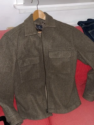 Grå overshirt med dragkedja - Stilren grå overshirt från H&M  med rak passform och två bröstfickor med lock. Dragkedja framtill och klassisk krage ger en clean look. Perfekt lager på lager-plagg för dig som gillar minimalistisk stil.