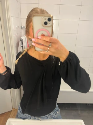 Svart långärmad body - Stilren svart blus med långa, lösa ärmar och en snygg draperad detalj framtill. Blusen har rund halsringning och är gjord i ett tunt, mjukt material som ger ett elegant fall. Skriv vid frågor och pris kan diskuteras!💕💕