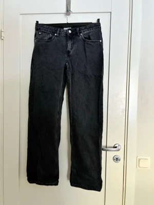 Svarta raka jeans med fem fickor - Säljer ett par svarta jeans med rak passform och klassisk femficksdesign. Jeansen har normal midja, bälteshällor och silverfärgade nitar. Materialet är kraftig denim i bomull. Perfekta för en avslappnad och stilren look. Tror modellen heter Icon från lager 157. Aldrig använda endast legat i garderoben❤️