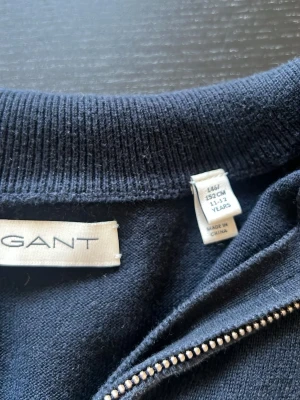 Marinblå halvzip-tröja från Gant - Snygg marinblå tröja från Gant med halv dragkedja och diskret logga på bröstet. Tröjan har ribbade muddar vid ärmslut och nederkant samt en klassisk krage med vita detaljer.