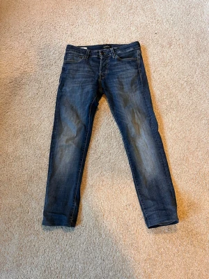 Jack and jones - Snygga mörkblå slim fit jeans med klassisk femficksdesign och lätt slitna detaljer på benen. Jeansen har normal midja och raka ben, perfekta till en avslappnad stil. Tillverkade i stretchig denim för extra komfort.