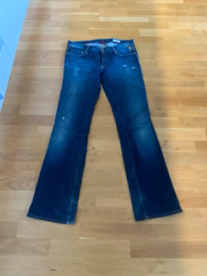 Mörkblå Replay bootcut jeans 30/32 - Säljer ett par mörkblå Replay bootcut jeans med slitningar och klassiska fem fickor. Jeansen har kontrastsömmar och lätt tvättade detaljer framtill och baktill. Materialet är denim och passformen är utsvängd nedtill. 