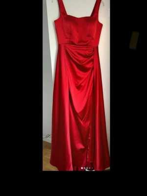 Röd  festklänning satin - En superfin festklänning i nyskick som är använd ett par timmar vid ett tillfälle Och därefter kemtvättad.   Klänningen är lång i längden och släpar lite på golvet. Jag som har haft klänningen är 175 cm lång. Står stl 44 i klänningen men den passar mig som väger cirka 78 kilo. 