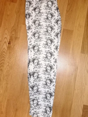 Vita byxor med fint svart mönster från H&M - Snygga vita byxor med svart cool mönster över hela tyget. Byxorna har smal passform och normal midja. Perfekta för dig som vill sticka ut med ett unikt print. Materialet känns mjukt och bekvämt mot huden. Har dragkedja på sidan och hällor för skärp. Byxan köptes på H&M och har knappt använts, är i toppen skick. 