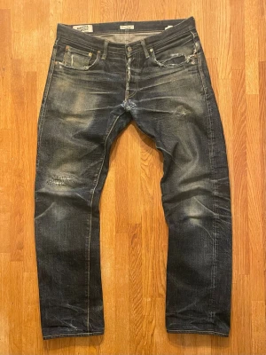 N&F selvedge jeans - Ett par mörkblå selvedge jeans från Naked & Famous Denim med slitningar och tvättade detaljer. De är lagade vid skrevet och knät. Mått på midja är 42cm, ytterbenslängd är 103cm, benöppning är 18,5cm.