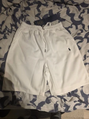 Vita shorts från Polo Ralph Lauren - Snygga vita shorts från Polo Ralph Lauren med klassisk broderad logga på benet. Shortsen har elastisk midja med snörning och sidofickor. Perfekta för sommaren och har en clean, sportig look.
