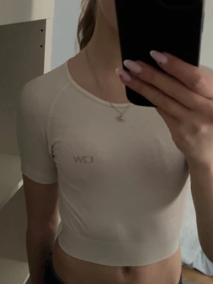 Vit träningstopp  - Vit croppadtränings topp från ICANIWILL med korta ärmar och rund hals. Toppen har en bred ribbad kant nedtill och diskret logga framtill.  Mjukt och stretchigt material!