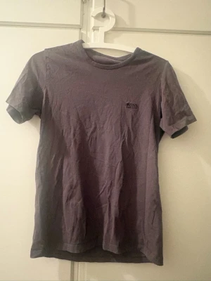 Mörklila t-shirt från BOSS - En stilren brun t-shirt från BOSS med diskret logga på bröstet. Klassisk passform med rund hals och korta ärmar. Tillverkad i mjuk bomull som känns skön mot huden. Perfekt t-shirt nu till sommaren.
