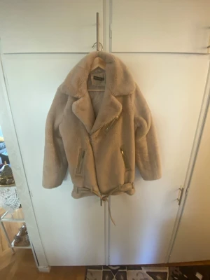 Beige teddyjacka med bälte och dragkedjor - Säljer en beige teddyjacka från Bik Bok med oversized krage, snedställd dragkedja och två fickor med dragkedjor. Jackan har ett bälte i midjan för extra stilpoäng och är gjord i mjukt teddy-material. Perfekt för kalla dagar när du vill vara både varm och trendig.