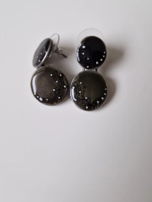 Svarta/ örhänge från franska IKITA  y2k - Unika örhängen med två runda plattor i svart och grått, dekorerade med små pärlliknande detaljer. Örhängena är emaljerade och har stift bak. Kommer från franska Ikita och är nya och från tidigt 2000-tal.  3 cm långa  y2k