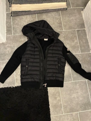 Svart pufferjacka med huva från Moncler - Moncler cardigan i storlek M. Scan funkar och även chippet i själva loggan, jag säljer den i gott skick inga konstigheter alls.