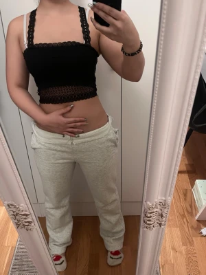 Svart spetsig croppad linnetopp - Snygg svart croppad linnetopp med breda spetsband och dekorativ spetsdetalj både fram och bak. Toppen har en unik rygg med spetsmönster som ger en extra touch. Perfekt att styla med jeans eller kjol för en trendig look.