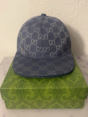 Blå GG-mönstrad keps från Gucci - Snygg blå keps från Gucci med klassiskt GG-monogram över hela kepsen. Kepsen har böjd skärm och är tillverkad i denimliknande material. Perfekt för dig som vill sticka ut med en exklusiv accessoar.