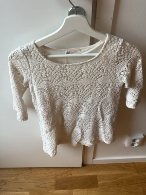 Vit virkad stickad tröja H&M stl 146 - Snygg vit stickad tröja från H&M med virkat mönster och trekvartsärmar. Tröjan har rund halsringning och är gjord i ett lätt och luftigt material, perfekt för lager-på-lager-stil.