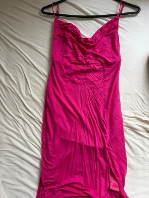 Mini tight Rosa långklänning med öppen rygg - Säljer en snygg rosa långklänning med tunna axelband och draperad urringning. Klänningen har en smickrande passform och är tillverkad i ett mjukt, följsamt material som känns bekvämt mot huden. Perfekt för dig som vill sticka ut med färg.