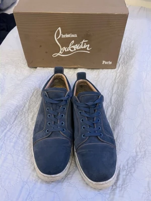 Blåa sneakers från Christian Louboutin - Snygga blåa sneakers från Christian Louboutin i mocka med klassisk låg siluett och matchande blå skosnören. Skorna har en vit sula och diskreta sömdetaljer som ger en clean look. Perfekta för dig som vill ha något exklusivt och stilrent.