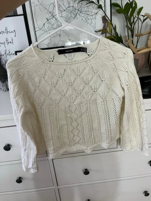 Vit stickad tröja från Vero Moda - Snygg vit stickad tröja från Vero Moda med ett detaljerat hålmönster och rund halsringning. Tröjan har långa ärmar och en något kortare, boxig passform. Perfekt att styla med jeans eller kjol för en trendig look.