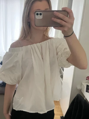 Vit offshoulder blus från H&M - Säljer en vit offshoulder blus från H&M i storlek S. Blusen har puffiga korta ärmar och en lös passform med resår vid axlarna. Perfekt för dig som gillar romantisk och trendig stil. Materialet känns lätt och luftigt.