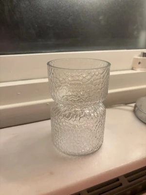 Unikt glas med strukturmönster - Säljer ett coolt glas i klart glas med ett unikt strukturmönster som påminner om is eller bikakor. Glaset har en ovanlig form med en smal midja i mitten och bredare topp och botten.