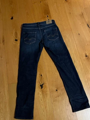 Mörkblå jeans från Replay - Snygga mörkblå jeans från Replay med raka ben och klassiska bakfickor med dekorativa sömmar. Perfekta för dig som gillar en enkel men trendig stil. Passar även i storlek 27. Är i storleken 14y.