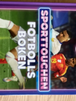 Sporttouchen Fotbollsboken - En färgstark bok om fotboll med omslag i lila, grönt och rött. Boken har hårda pärmar och är skriven av Tim Rangström, Charles Faro och Jesper Tillberg. Perfekt för dig som vill läsa mer om fotbollens värld och få inspiration från sporten.