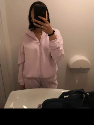 Ljusrosa mjukisdress med dragkedja /Lululemon  - Säljer en Lululemon ljusrosa loungewear-set med zip hoodie och matchande byxor. Setet har avslappnad passform, långa ärmar och resår i midjan. Perfekt för chill dagar hemma eller när du vill vara bekväm men ändå se söt ut. Materialet känns mjukt och skönt mot huden.