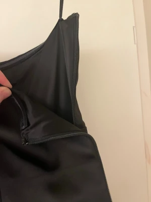 Svart satin korsettopp med dragkedja - Snygg svart korsettopp i satin med hjärtformad urringning. Toppen har en markerad midja och dragkedja och hyskor i sidan för enkel på- och avtagning. Perfekt för att skapa en trendig look. Helt oanvänd med prislapp , nypris 799 kr