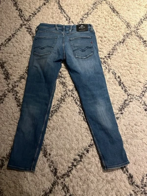 Blå slim fit jeans från replay - Snygga blå slim fit jeans med klassiska bakfickor och diskreta slitningar. Jeansen har normal midja och raka ben, tillverkade i ett mjukt denimtyg som ger en bekväm känsla. Perfekta för en avslappnad och trendig stil.