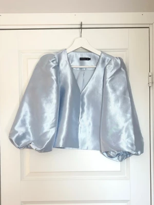 Ljus blå blus med puffärmar MQ - Supersnygg ljusblå blus från Stockh LM MQ med glansigt material och v-ringning. Blusen har stora puffiga långärmar och en rak. Storlek 34/XS🤍 Aldrig använd.