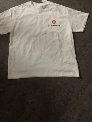 Vit t-shirt från Casablanca - Vit t-shirt från Casablanca med liten logga och text på bröstet. Klassisk passform och rund halsringning. Perfekt basplagg för en clean och stilren look.