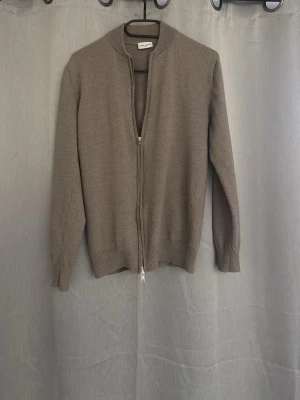 Beige ziptröja från John Henric - Snygg beige ziptröja från John Henric i mjukt stickat material. Tröjan har hel dragkedja, ribbade muddar och en stilren, enkel design som passar perfekt till lager-på-lager. Perfekt för dig som gillar en clean och klassisk look.