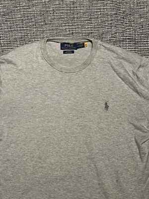 Grå långärmad tröja från Polo Ralph Lauren - Snygg grå långärmad tröja från Polo Ralph Lauren med klassisk rund halsringning och broderad logga på bröstet. Tillverkad i mjukt bomullsmaterial som är skönt mot huden. Perfekt för en avslappnad och stilren look.