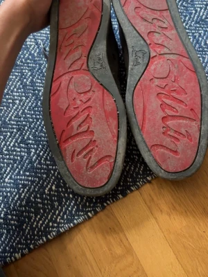 Grå loubs  - Snygga grå mockaskor från Christian Louboutin med ikonisk röd sula och diskret logga på insidan. Skorna har en stilren design och är tillverkade i mjuk mocka med svarta detaljer. Perfekta för dig som vill sticka ut med exklusiva detaljer.