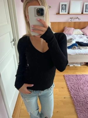 Svart ribbad stickad tröja Amisu - Säljer en svart ribbad stickad tröja från Amisu med v-ringning och långa ärmar. Tröjan är figurnära och har en mjuk, stretchig känsla som passar perfekt till jeans eller kjol. Enkel och stilren design som funkar till många olika looks.