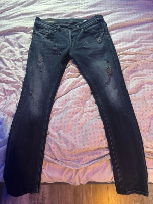 Mörkblå  jeans från Dondup - Snygga mörkblå jeans från Dondup med slitningar och distressed detaljer på benen. Klassisk femficksmodell med smal passform och låg midja. Tillverkade i denim med stretch för extra komfort. Längd: 103cm, modellen är 193cm lång och växer cirka 80kg, de är något för breda i storleken därav säljs de. Nypris 4000kr!